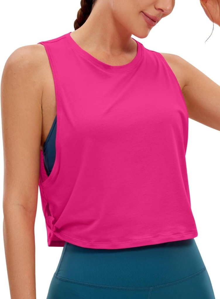 Laad afbeelding in Galerijviewer, Persoon gekleed in een roze &quot;Stijlvol en comfortabel: Yoga dames pima cotton workout tank crop&quot; en een blauwgroene legging, poseert sierlijk met één hand op het hoofd.
