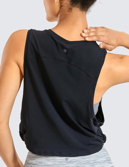 Een persoon draagt de "Stijlvol en comfortabel: Yoga dames pima cotton workout tank crop" in het zwart, met daaronder een lichtgrijze sportbeha. De beha raakt de schouder aan en het gezicht is van de persoon afgekeerd.