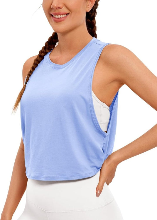 Een persoon draagt een lichtblauwe "Stijlvol en comfortabel: Yoga dames pima cotton workout tank crop" en een witte broek, glimlachend met gevlochten haar.