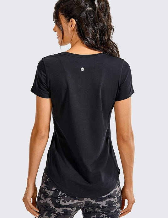 Een persoon draagt een Perfecte yoga t-shirt voor elke workout, in het zwart en een legging met camouflagemotief, met het gezicht van de ander af.