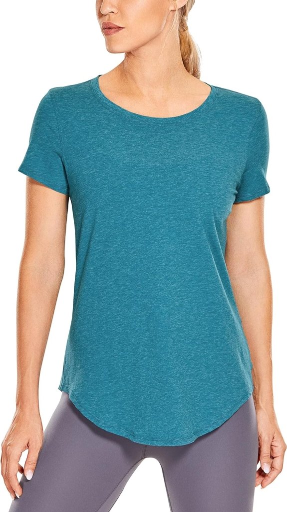 Laad afbeelding in Galerijviewer, De persoon draagt het Perfecte yoga t-shirt voor elke workout in de kleur blauwgroen, met korte mouwen en gemaakt van Pima katoen, gecombineerd met grijze leggings, tegen een witte achtergrond.
