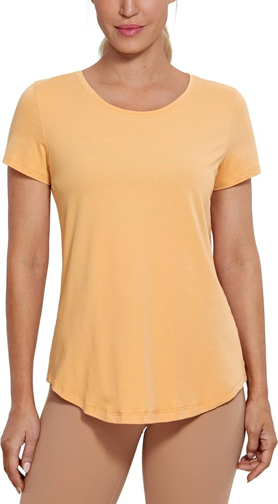 Laad afbeelding in Galerijviewer, Een persoon is gekleed in een lichtoranje &quot;Perfecte yoga t-shirt voor elke workout&quot; met een beige broek.
