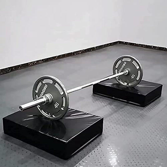 Een halter met gewichten geplaatst op twee zwarte platforms met halterpads: de ultieme bescherming voor je halter en vloer, op een grijze tegelvloer in een sportschool.