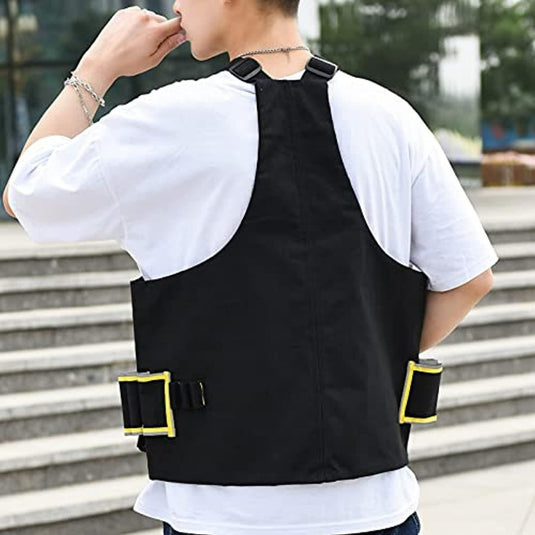 Een man, gekleed in een wit t-shirt en een zwarte anti-diefstal borsttas voor fitness met gele bandjes, van achteren gezien, staande op een buitentrap tijdens zijn fitnessroutine.