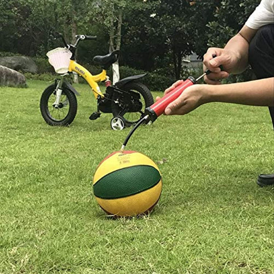 Een persoon blaast een gele en groene basketbal op met het Geniet overal van je spel met de draagbare ballenpomp, vlakbij een kleine gele fiets op een grasveld.