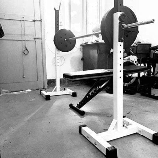 Zwart-wit beeld van een ultieme tool voor krachttraining en halterset in een garage-gym met betonnen vloeren en apparatuur verspreid.