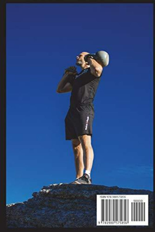 Een man staat op een rots en tilt een Kettlebell Workouts and Challenges 1.0 kettlebell boven zijn hoofd tegen een helderblauwe lucht tijdens zijn kettlebell-trainingen.
