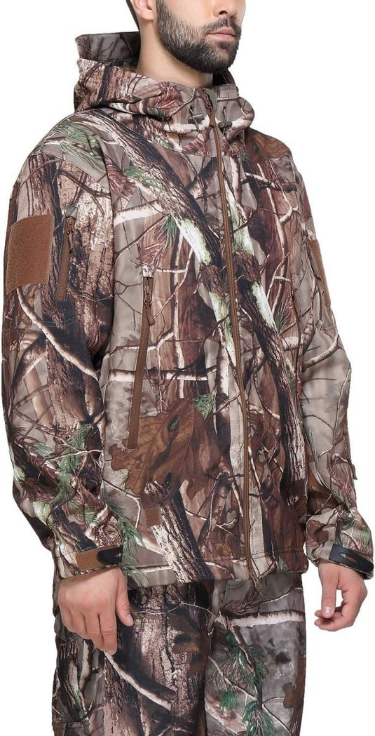 Man met een Camouflage tactische heren softshell jas met capuchon, voorzien van een bosmotief en een bruine patch op de mouw. Deze heren softshell jas is bovendien ademend en waterdicht.