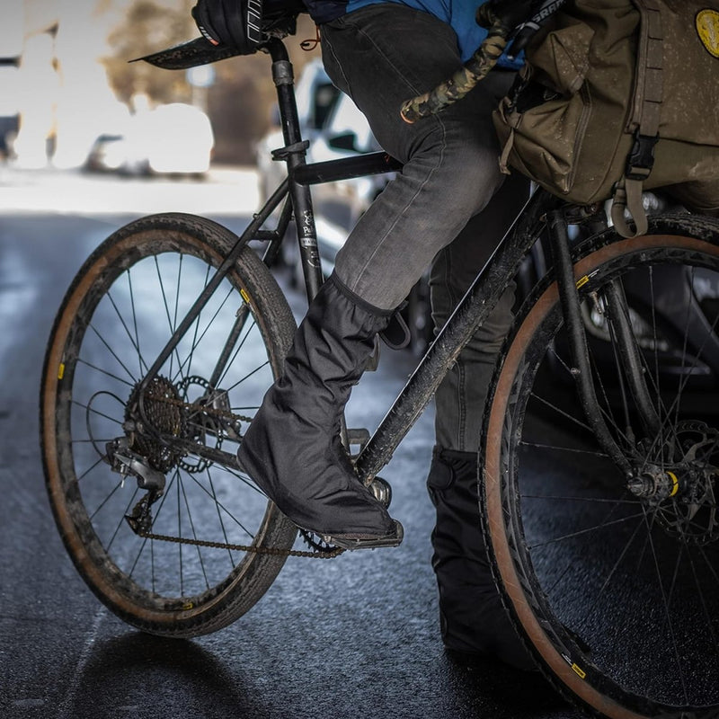 Load image into Gallery viewer, Een fietser die op zijn fiets stapt en zich concentreert op de voet die van de grond afzet, met Regenoverschoenen voor fietsers: blijf droog en stijlvol.

