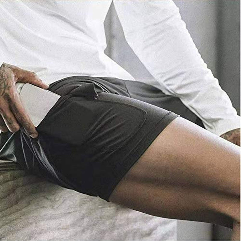 Load image into Gallery viewer, Een persoon die op bed zit en een mobiele telefoon uit de tailleband van zijn zwarte broek haalt Ontdek het ultieme comfort en de functionaliteit van onze heren 2-in-1 shorts.
