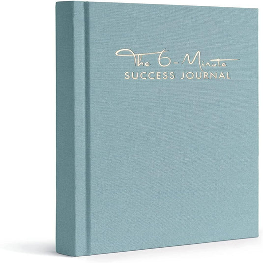 Een lichtblauw dagboek met de titel "Het 6-Minute Success Journal: Transformeer je Leven met Slechts 6 Minuten Per Dag!" rechtopstaand weergegeven met een gestructureerde omslag, gericht op het verbeteren van de productiviteit.