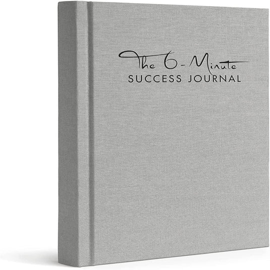 Een grijs hardcover boek met de titel "Het 6-Minute Success Journal: Transformeer je Leven met Slechts 6 Minuten Per Dag!" rechtopstaand weergegeven met een gestructureerde omslag, ontworpen om de productiviteit te verhogen.
