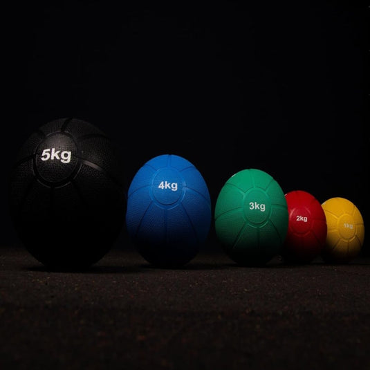 Vijf Trein je lichaam met de medicijnbal van verschillende gewichten en kleuren in oplopende volgorde van links naar rechts.