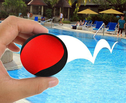 Hand met een Waterballen: een waterpret voor het hele gezin, die een deel van een levendig tafereel bij een zwembad beslaat met loungende mensen en een hotel op de achtergrond.