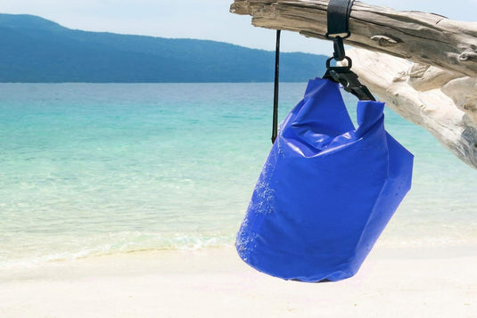 Een blauwe Houd je waardevolle spullen veilig en droog met onze waterdichte tas die aan een boom op een strand hangt en bescherming biedt voor buitenavonturen.
